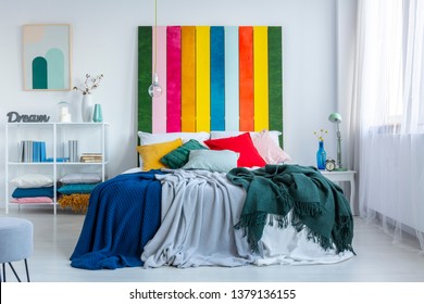 Green, Gray And Blue Blankets On A White Bed With Rainbow Bedhead In White, Scandi Bedroom Interior. Real Photo