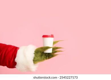 Green hairy hand of creature in Santa costume with coffee on pink background - Powered by Shutterstock