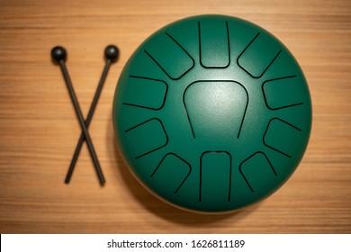 Green Hand Pan Steel Tongue Drum Musical Instrument With 11 Notes And A Pair Of Drum Hammer On A Wooden Background