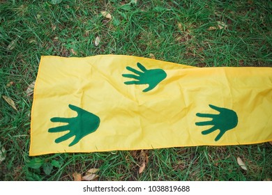 Green handprints on yellow long fabric on green grass. Playgame. Closeup.
