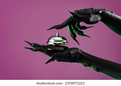 Green hands of witch with hotel bell on purple background. Halloween celebration