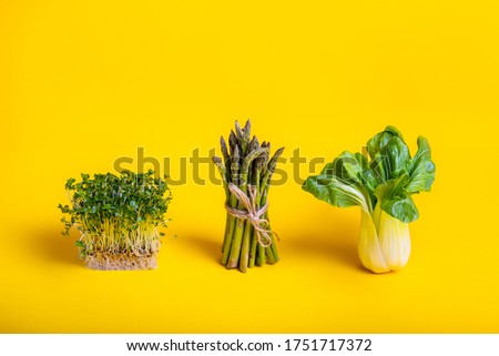 Green healthy food on yellow background. Pak Choi, asparagus and fresh sprouts of Water Cress salad. Vegetarian and vegan diet. Veganism. Sustainable lifestyle, good eats, plantbased foods. Copy space