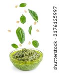 Green healthy homemade italian pesto sauce served in glass bowl with flying or levitating ingredients such as fresh basil leaves, pine nuts, olive oil, garlic and parmesan isolated on white background