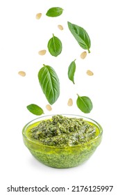 Green healthy homemade italian pesto sauce served in glass bowl with flying or levitating ingredients such as fresh basil leaves, pine nuts, olive oil, garlic and parmesan isolated on white background