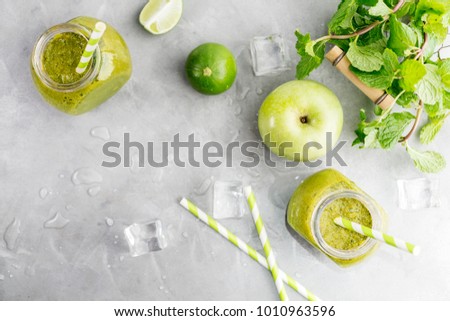 Green healty drink in mason jar with green apple, mint, lime and melting ice cubes on grey background. Vegetarian food concept. Detox. Text space