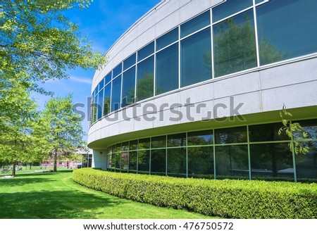 Green hedge and mowed lawn along round shaped wall of the office building