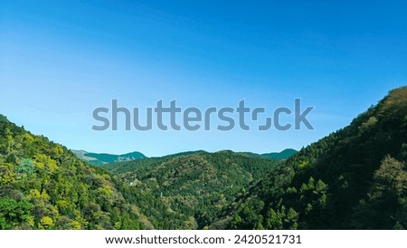 Green hills in Japan, morning, featuring a mountain landscape with trees in autumn colors green yellow orange under a clear blue sky, epitomizing serene natural beauty. SHOTLISTtravel