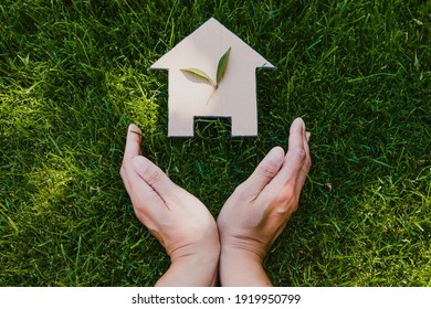green home and eco-friendly construction conceptual image, house icon on green grass lawn under the sun with two leaves on top and hands framing it