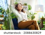 Green Home. relaxed stylish woman with long wavy hair at modern home in sunny day in green pants and grey blouse sitting in a blue armchair.
