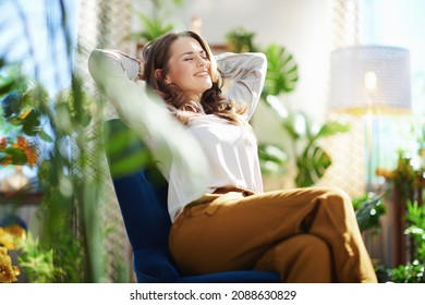 Grünes Zuhause. Entspannte stylische Frau mit langen Haaren im modernen Zuhause an sonnigen Tagen in grüner Hose und graue Bluse sitzend in einem blauen Sessel.