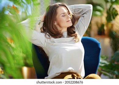Green Home. relaxed trendy 40 years old housewife with long wavy hair at modern home in sunny day in green pants and grey blouse sitting in a blue armchair.