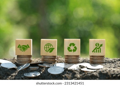 Green icons on wooden cubes on money coin stack. Green business growth. Finance sustainable development.growing money, finance and investment. Alternative sources of energy. Eco business investment - Shutterstock ID 2313421451