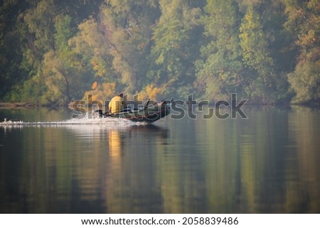 Green inflatable rubber motor boat floating on the river for fishing on autumn trees background