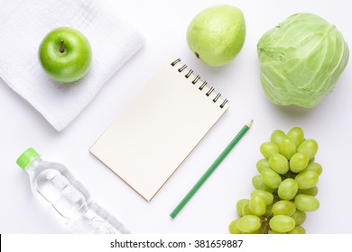 Green items. Fitness concept with bottle of water, notebook, towel, green apple and fruits over wooden background. View from above - Powered by Shutterstock