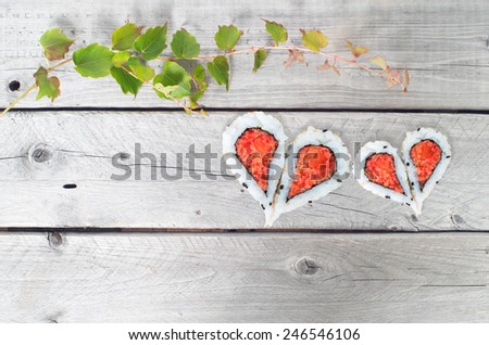 Green ivy vine and two hearts shape forming from four pieces of sushi on a vintage wooden table