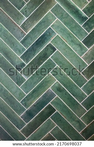 Green and jade handmade retro tiles in a herringbone pattern on the wall of a shower. 
