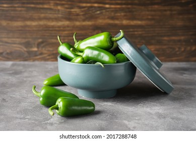 Green jalapeno peppers in a ceramic bowl on a gray-wooden background.