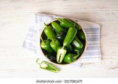 Green jalapeno peppers in a wooden plate on a wooden background, top view.