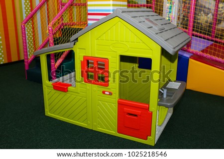 Green kids playhouse in the entertainment center. Plastic children play house with red and orange door and window. Green floor. Joy and fun. Playing games.