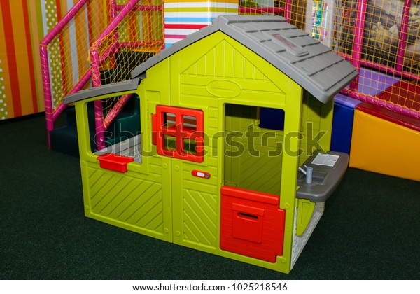 Green kids playhouse in the\
entertainment center. Plastic children play house with red and\
orange door and window. Green floor. Joy and fun. Playing\
games.