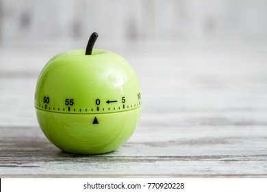 Green kitchen cooking timer with apple shape on white wooden background