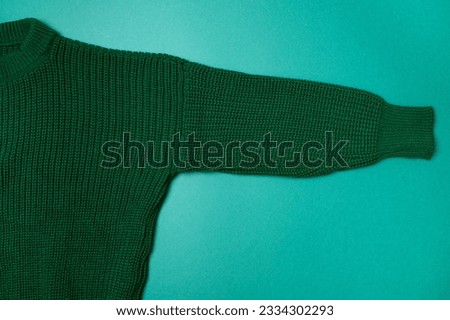Green knitted sweater on paper green background top view copy space. Texture of woolen cotton winter autumn cozy sweater, clothes. Knitted jumper, pullover, fashion. Sweater close-up