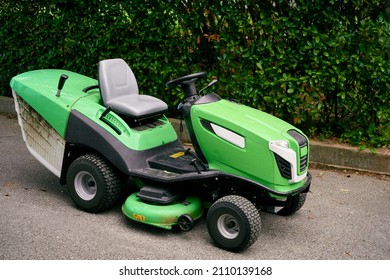 Green Large Lawn Mower Stands On The Asphalt Near The Bushes