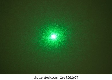 A green laser beam's diffraction pattern, creating a starburst effect with a bright central spot on a dark background.