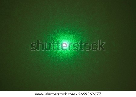 A green laser beam's diffraction pattern, creating a starburst effect with a bright central spot on a dark background.