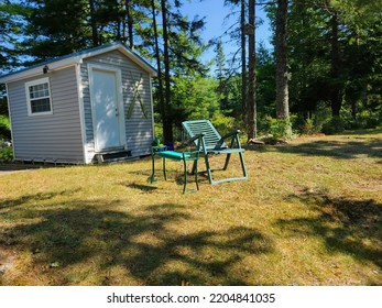 A Green Lawn Chair And Table Setup Outside Of A Shed In A Yard.