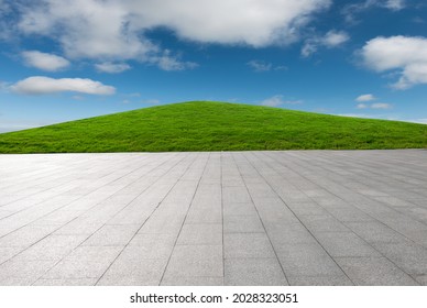 The green lawn hillside behind the stony plaza under a clear sky