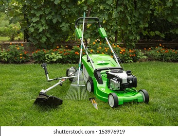 Green lawnmower, weed trimmer, rake and secateurs in the garden.