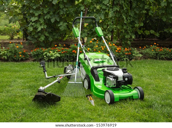 Green lawnmower, weed trimmer, rake and secateurs\
in the garden.