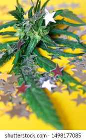 The Green Leaves Of Wild Cannabis Hemp And Silver Festive Confetti Stars Are On A Bright Yellow Background. Psychotropic Substances Used In Medicine. Party And Relaxation. Shallow Depth Of Field.