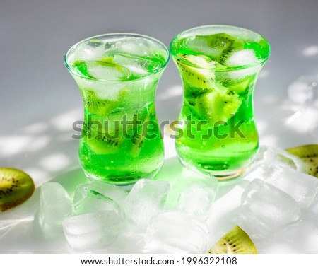 Green lemonade with ice and kiwi slices.Two glass glasses stand on the table and the sun's rays fall on them. Beautiful shadow and glare from the sun. Summer refreshing cool drink.