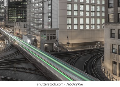 Green light streaks at train intersection with buildings in background