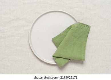 Green linen napkin on a clean beige plate, beige textile background. Top view, flat lay. - Shutterstock ID 2195925171