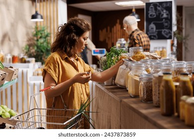 Green living woman in zero waste store interested in purchasing bulk products with high nutritional value. Client does pantry staples shopping in sustainable local neighborhood supermarket - Powered by Shutterstock