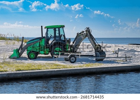 Green loader on white sandy beach using back hoe arm to secure boat trailer and prevent it from being stolen.