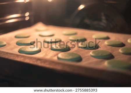 Green macaron shells baking on parchment paper inside oven, warm light and shallow depth of field, pastry process and homemade dessert preparation.
