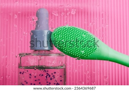 A green massager or silicone facial brush, cosmetic spatula on pink background. Beauty blog, hygiene products. Moisturizing serum bottle for skin care, essential oil. Makeup face care. Barbie concept.