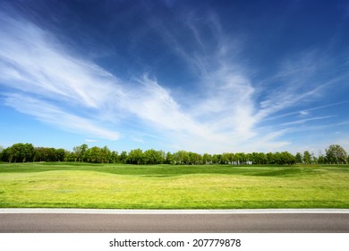 Green meadow and blue sky with asphalt road on foreground. Landscape in summer sunny day. 