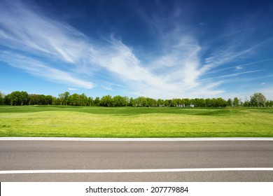 Green Meadow With Trees And Asphalt Road, Blue Sky On Background