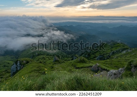 Green meadows with rocks and rocky mountains with fog in the valley and clouds in the sky in romanian mountains in muntii ciucas