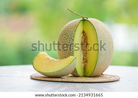 Green Melon on blurred greenery background, Cantaloupe Melon fruit in Bamboo mat on wooden table in garden.