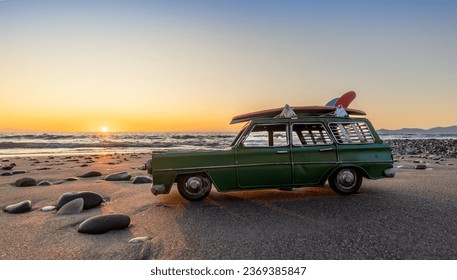 Green metal model surfing wagon at the beach water front, with a warm sunset sky.