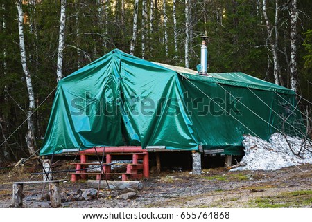 Green military tent with ladder at forest background as equipment for tourist camping.