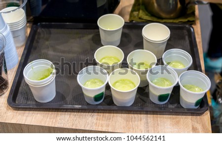 Green milke tea sample in mini white plastic tasting cup on black tray. Marketing promotion for new launched flavor of healthy product.