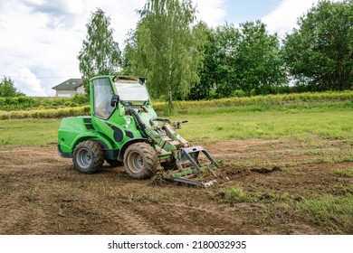 A Green Mini Skid Steer Loader Clear The Construction Site. Land Work By The Territory Improvement. Small Tractor With A Ground Leveler For Moving Soil, Turf. Machine For Agriculture Work. Copy Space.