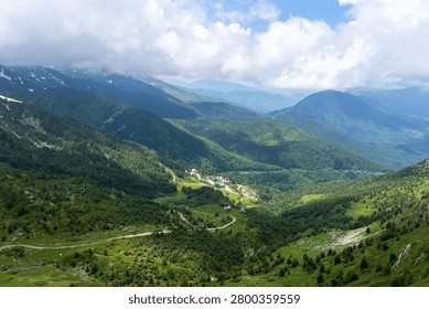 Green mountain landscape with sparse trees and distant peaks under a vibrant blue sky